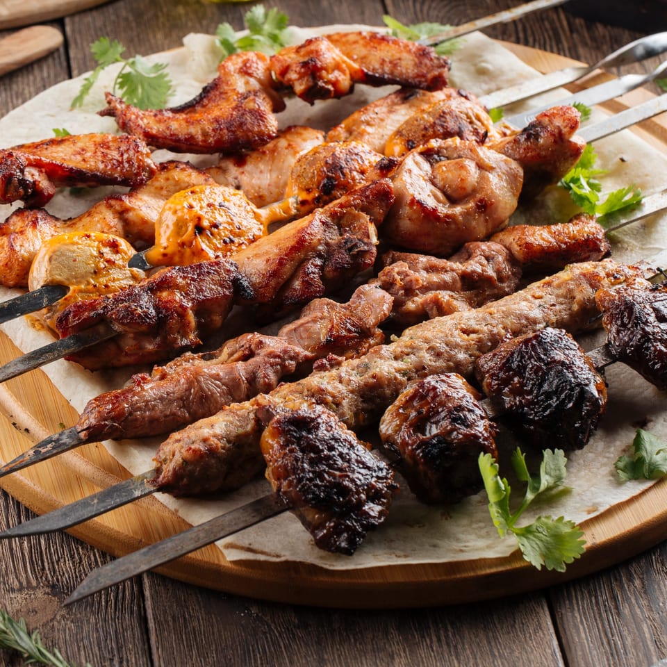 Assortment of Mediterranean grilled chicken wings, chicken pieces, and various kebabs on skewers.