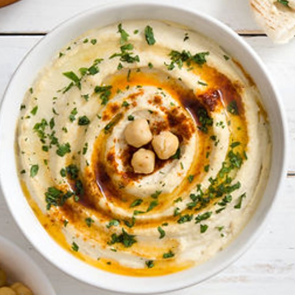 Creamy Mediterranean hummus in a white bowl, garnished with olive oil, paprika, chickpeas, and parsley.