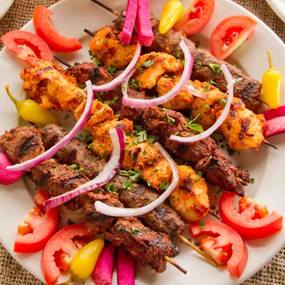 Platter of Mediterranean chicken and beef kebabs with tomatoes, pickled radishes, and onions.