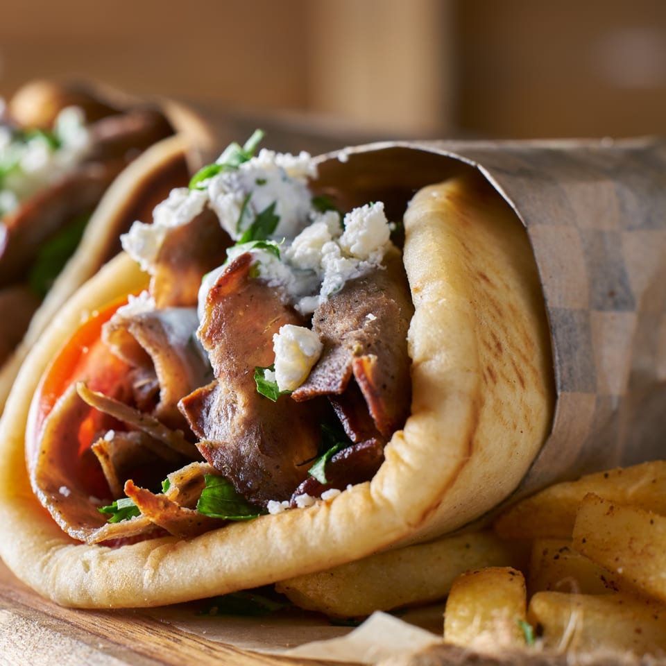 Close-up of a Mediterranean gyro with meat, tomatoes, feta, and herbs, wrapped in pita bread.