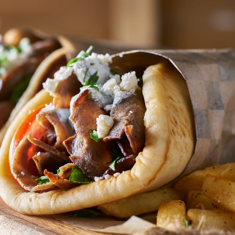 Close-up of a Mediterranean gyro with meat, tomatoes, feta, and herbs, wrapped in pita bread.