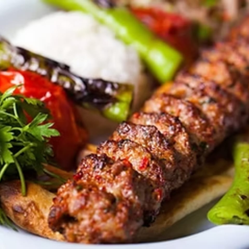Mediterranean kofta kebab with rice, grilled peppers, tomatoes, and parsley on flatbread.