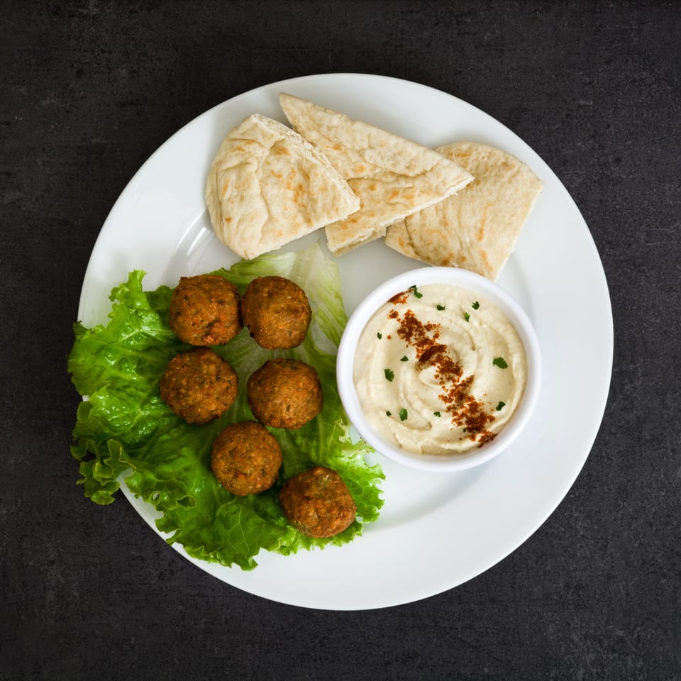A white plate with falafel on lettuce, hummus with paprika, and pita bread wedges.
